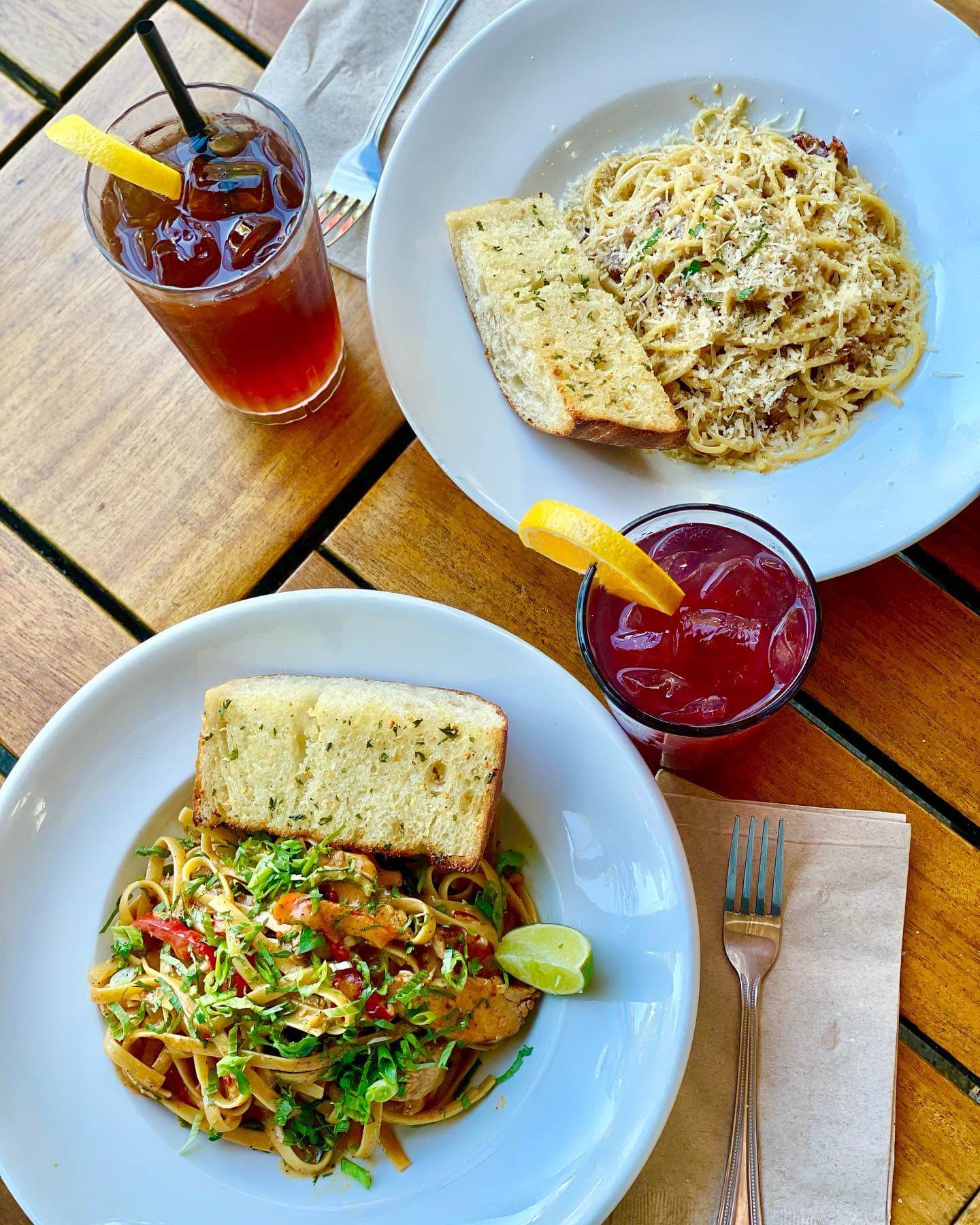 Two plates of pasta and garlic bread with two glasses of sangria.